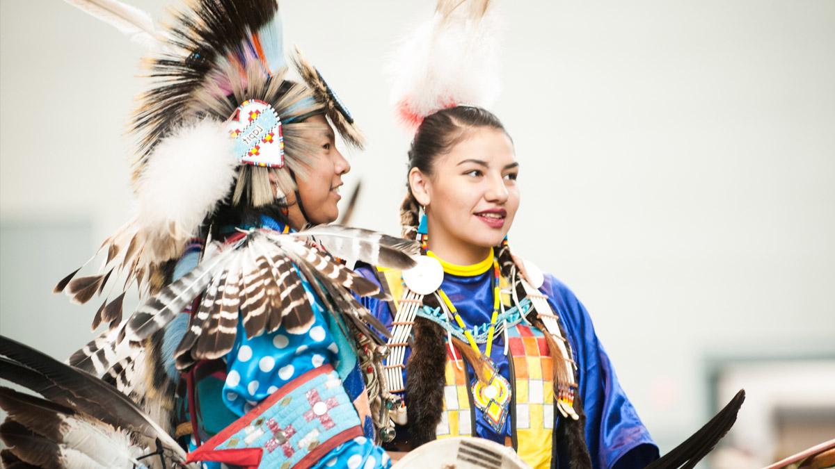 Two Native Americans wearing ceremonial garb.